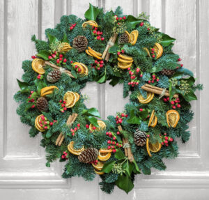 Round Christmas Door Wreath made with a variety of greenery on a grey door